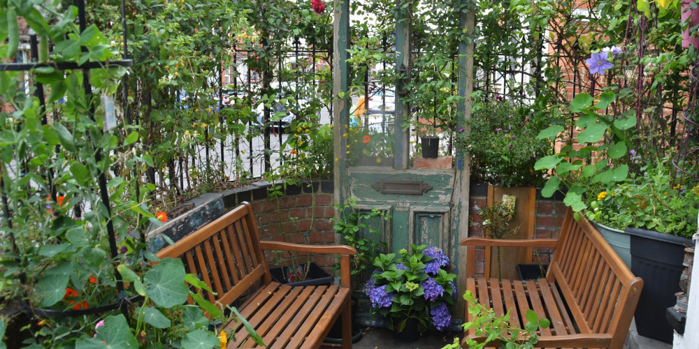 A picture of a garden seating area with benches, flowers, plants and an old door being used as decoration