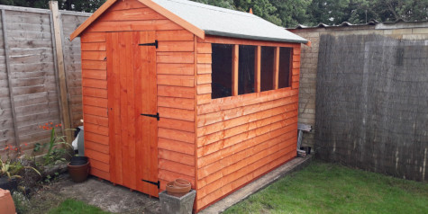 A picture containing a timber garden shed, fence, grass