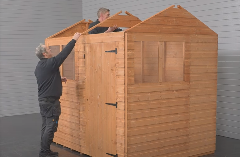A picture of two men dismantling a shed and removing an apex roof truss