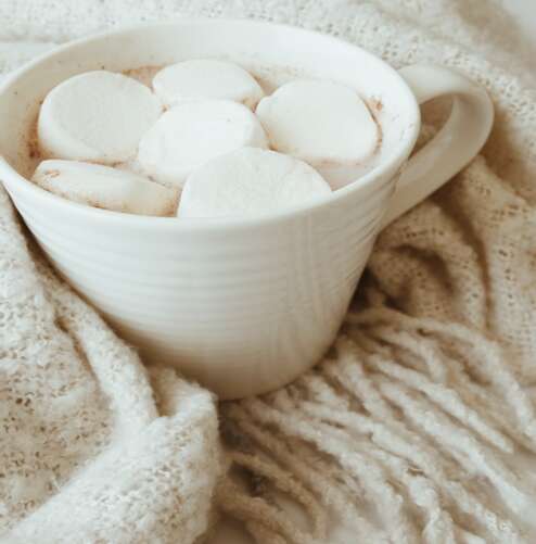 Hot Chocolate with Marshmallows in White Cup on Fluffy Cream Blanket