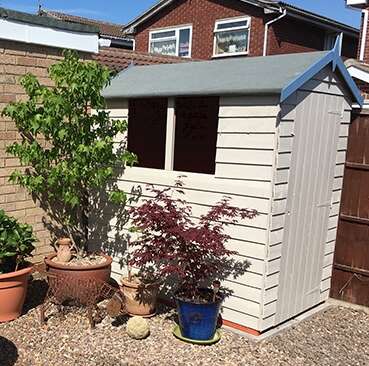 Tiger garden shed painted in cream with blue fascia boards on gravel patio with potted plants