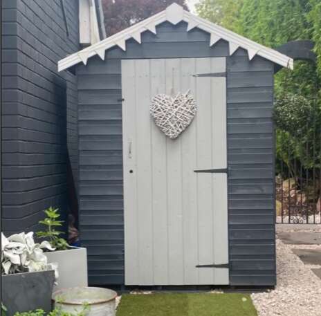 A Tiger Garden Shed painted in cream and grey with cream bunting in outdoor garden with grass and plants