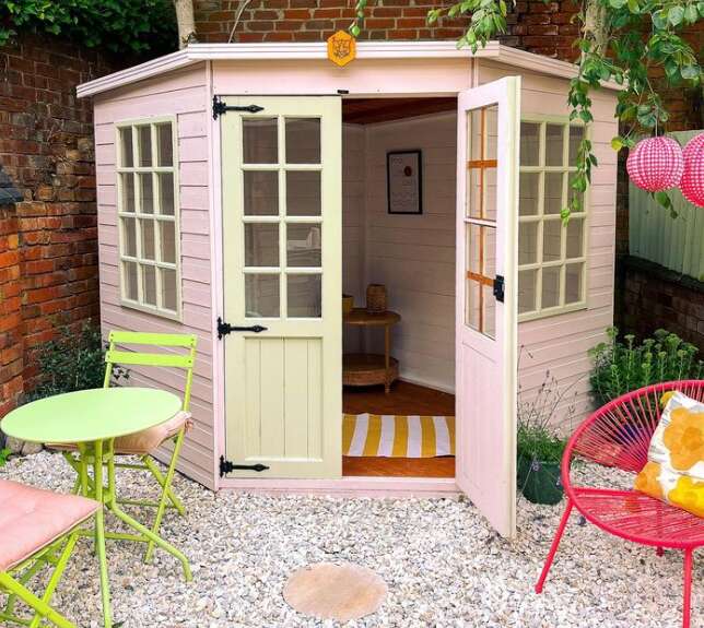 Tiger Corner Summerhouse painted in soft pink and grey with garden furniture and gravel path, plants