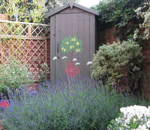 Tiger Tool Tower painted in brown with tree illustration with lavender and brick garden wall