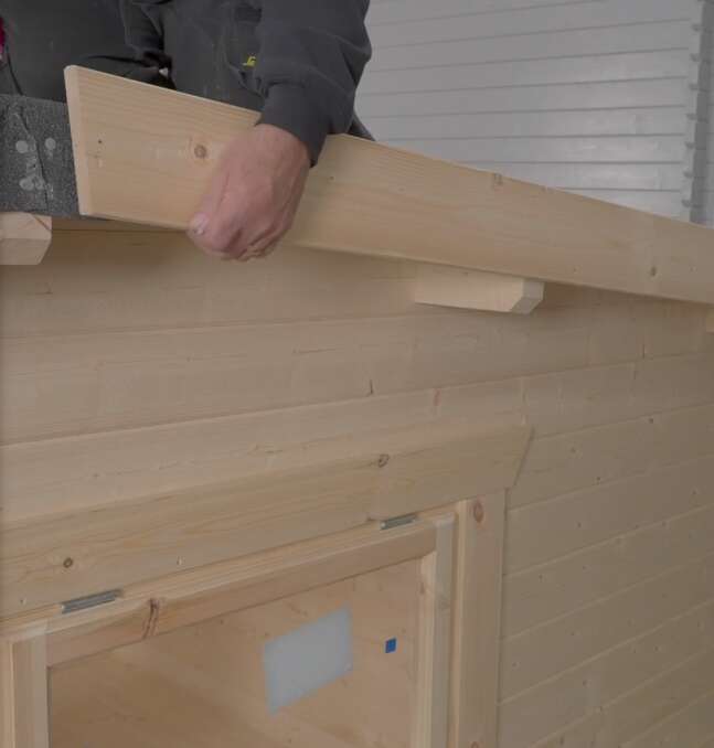 A picture containing person fitting fascia boards to roof felt on log cabin