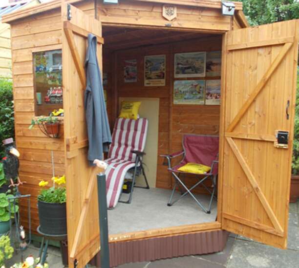 Tiger Deluxe Corner Shed, wooden garden room, deck chairs and posters on shed wall with potted yellow flowers