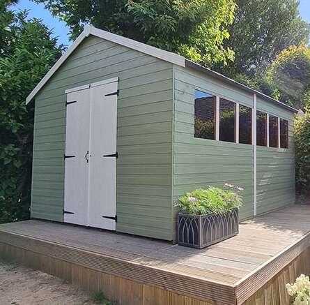Tiger Sheds Heavyweight Workshop painted in green and white in garden with trees and garden deck and plants