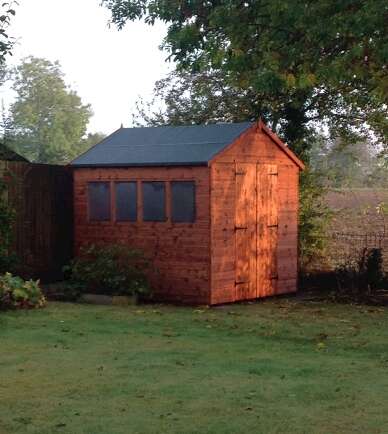 Tiger Shed Workshop in garden with double doors, windows, grass, fence and greenery