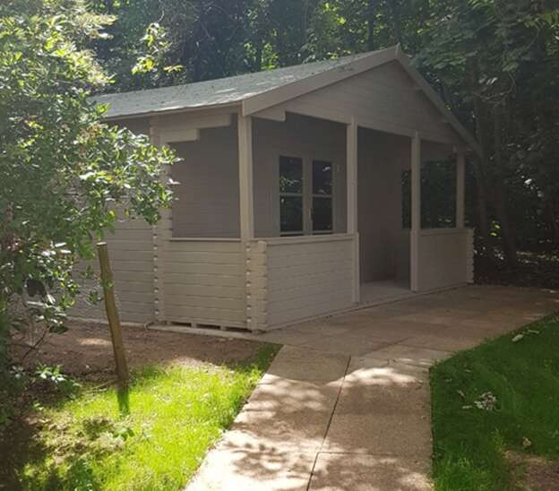 A picture containing the Tiger Sigma Log Cabin in garden setting with grass, trees and paved path leading to cabin