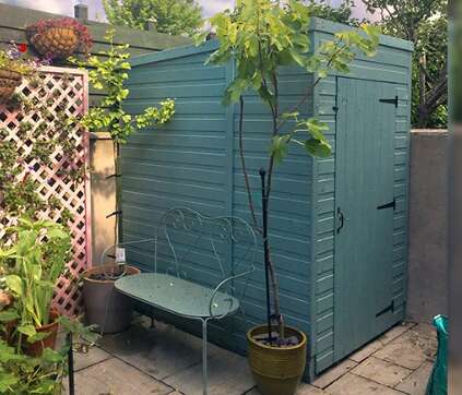 A picture containing a windowless pent garden shed with wooden bench and potted plants