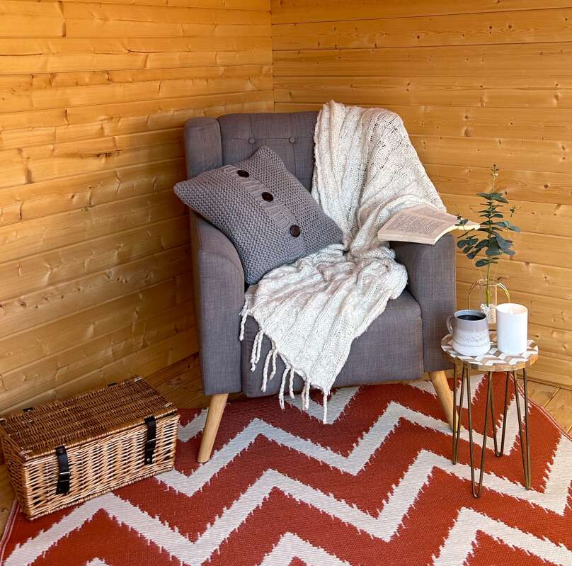 A chair with a blanket and a blanket on it, Tiger Sheds Vibrissa Log cabin interior. reading nook, home library