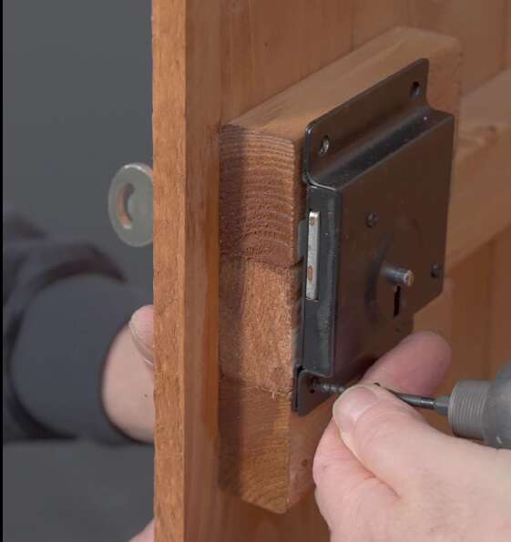 A person using a screwdriver to insert a door lock on a Tiger Shed