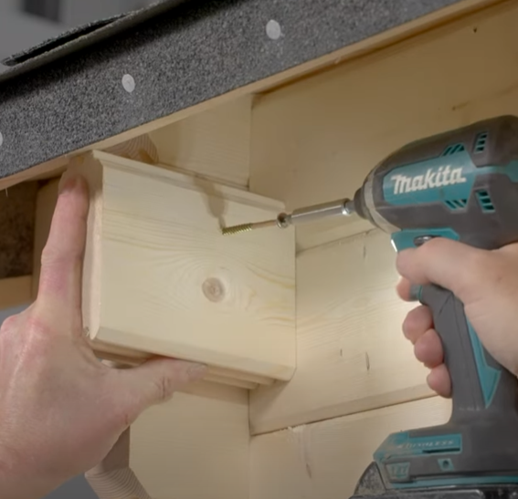 A picture of a man screwing a noggin into a log cabin