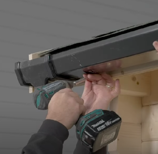 A picture of man securing guttering to a shed