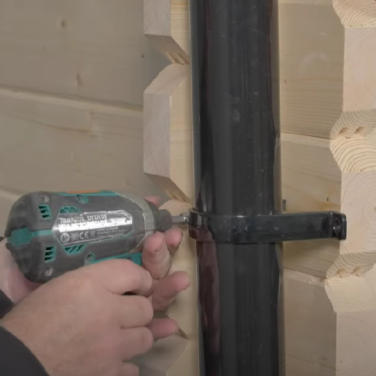 A picture of a man attaching a downpipe to a shed wall