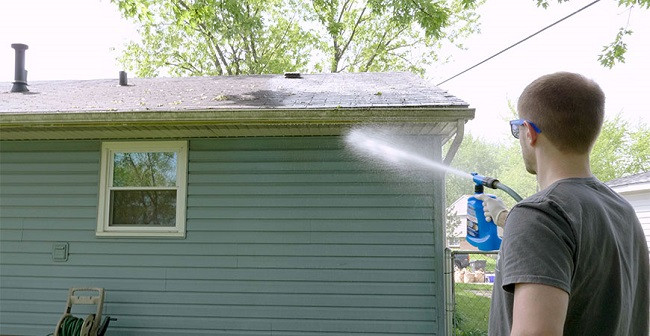 Man spray washing a shed